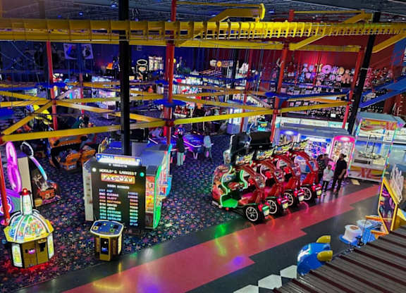 A carnival game room with a red car and a black game machine.