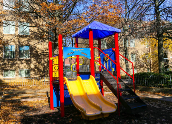 a playground with slides and a swing set in front of an apartment building