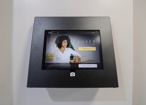 A black box with a screen displaying the word "LUXER" and a woman in the background.