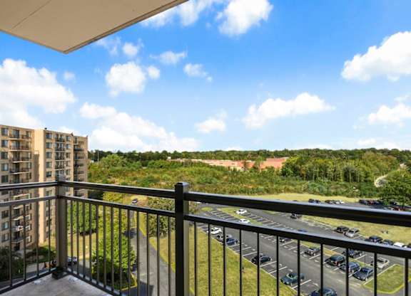 A balcony overlooks a parking lot and greenery.