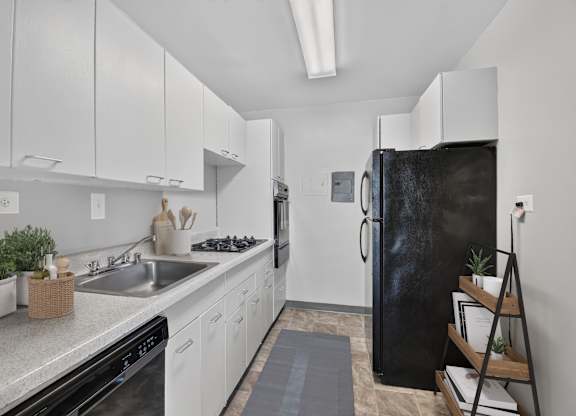 A black fridge in a white kitchen with a sink and a stove.
