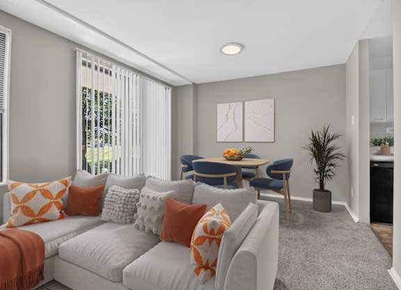 A living room with a grey couch, orange pillows, and a dining table with chairs.