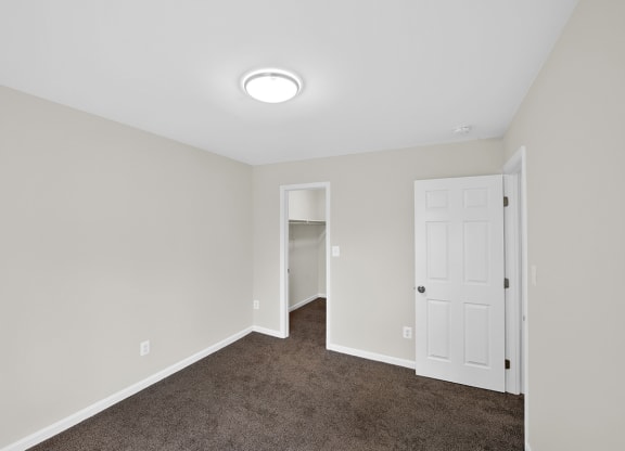 an empty bedroom with a white door and carpeted floor