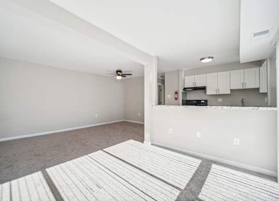 A spacious living room with a ceiling fan and a kitchen area in the background.