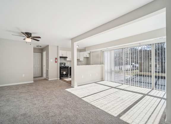 A spacious living room with a ceiling fan and a view of a parking lot through a sliding glass door.