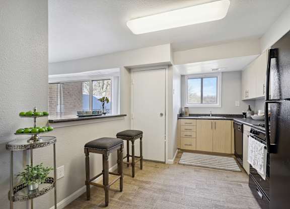 A kitchen with a black fridge, wooden bar stools, and a window with a view of trees.
