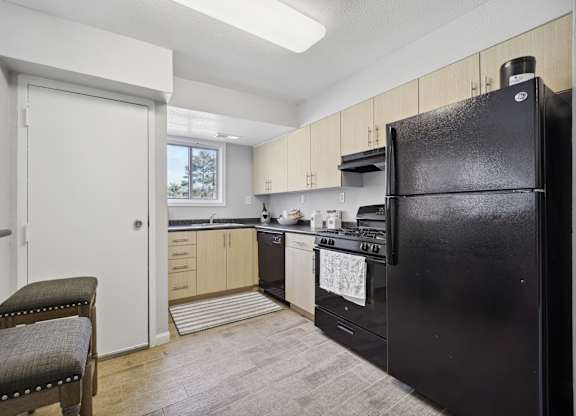 A black refrigerator is in a kitchen with wooden cabinets.