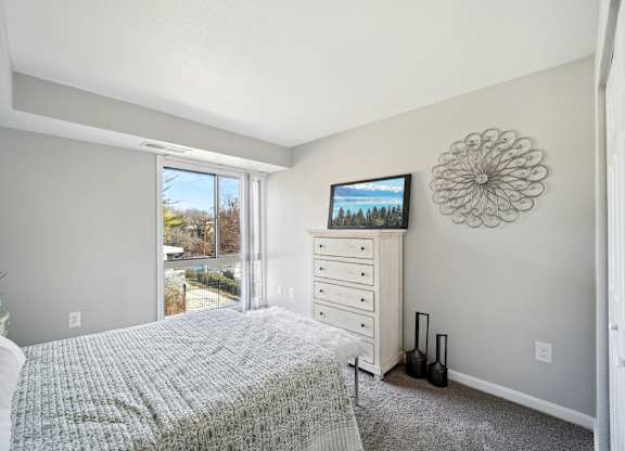 A bedroom with a bed, dresser, and a window overlooking a backyard.