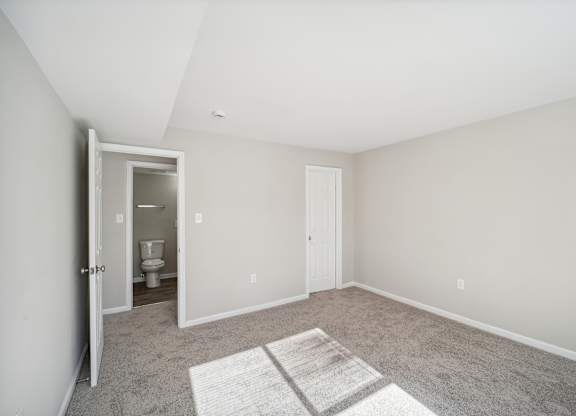 A room with a carpeted floor and a doorway leading to a bathroom.