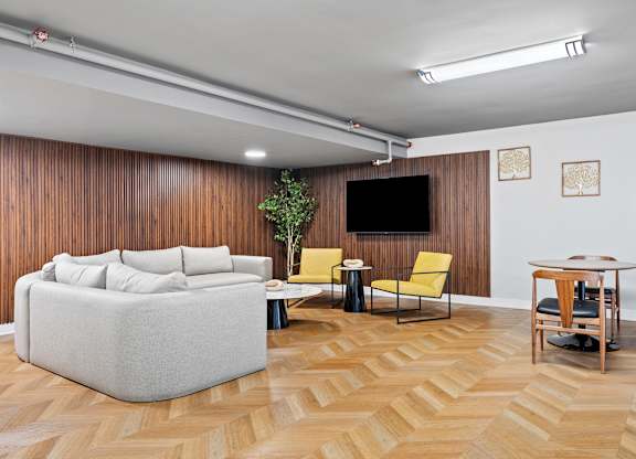 A living room with a grey sofa, a yellow chair, a small table, and a television.