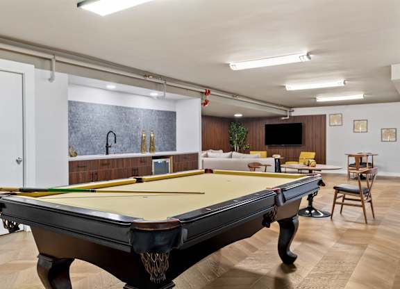 A pool table in a room with a bar and a TV.