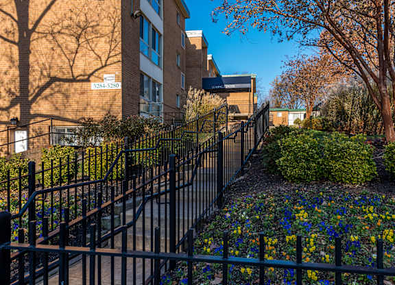 A black fence surrounds a flower bed in front of a brick building.