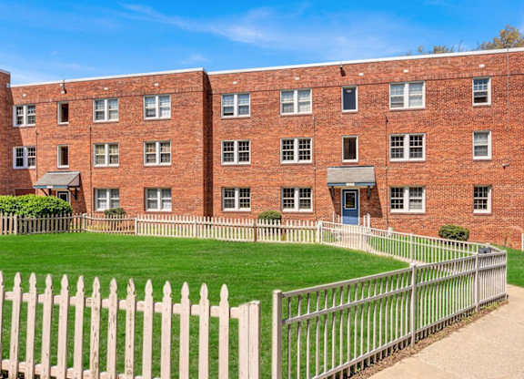 Red brick apartment building with white picket fence at Highland Ridge Apartments, Maryland