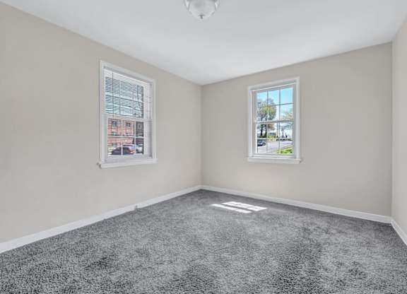 Empty bedroom with gray carpet and two windows at Highland Ridge Apartments, Capitol Heights