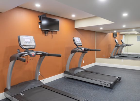 A gym with treadmills and a television mounted on the wall.