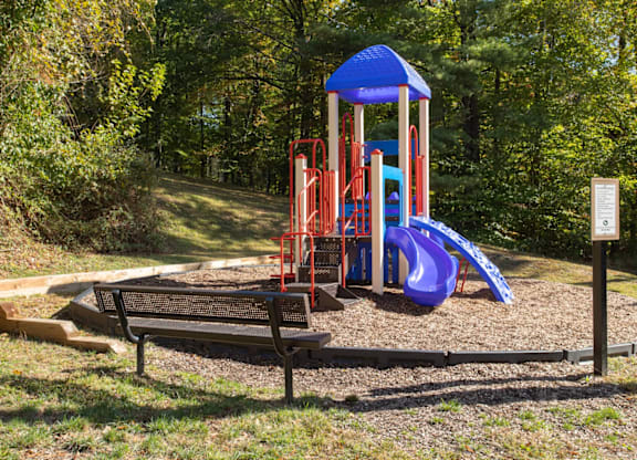 A playground with a blue slide and a wooden bench.