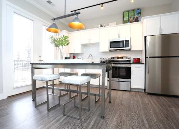 a kitchen with stainless steel appliances and a bar with three stools at Century Baxter Avenue, Louisville, 40204