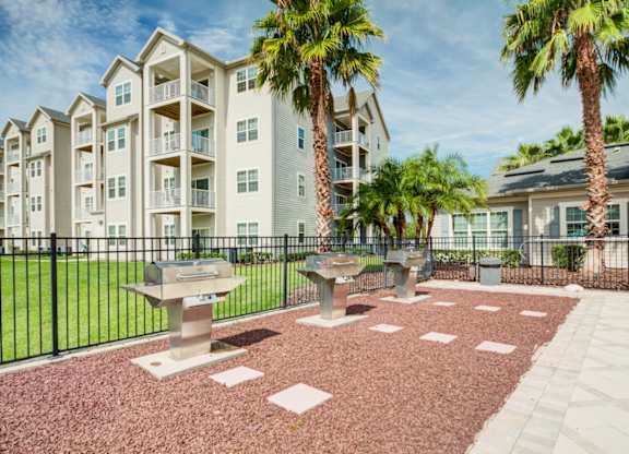a patio with three bbq pits and two palm trees in front of an apartment building  at Century Avenues, Florida, 33813