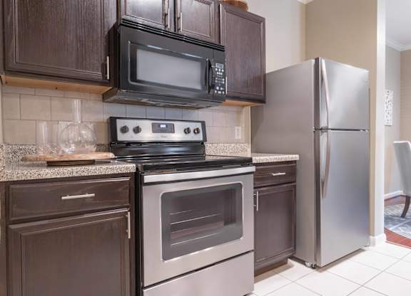 a kitchen with dark cabinets and stainless steel appliances at Century South Shore, League City
