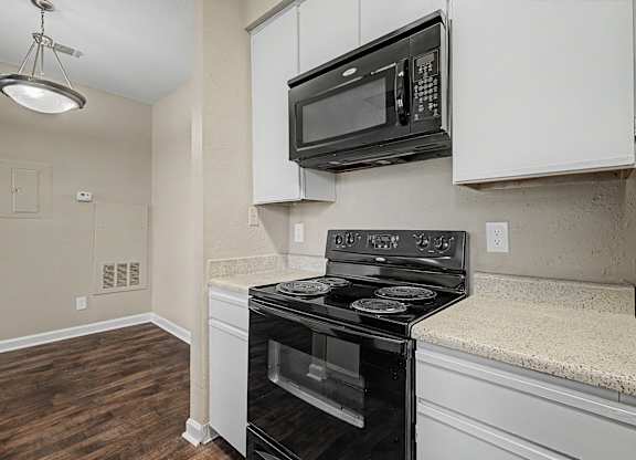 A black stove and microwave in a kitchen with white cabinets.