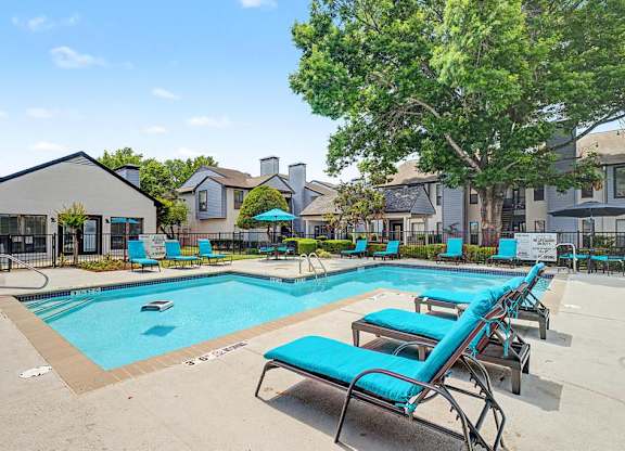 A swimming pool with blue loungers and a tree in the background.