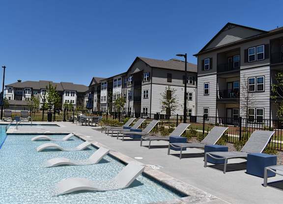 a swimming pool with lounge chairs in front of apartment buildings at Century Mundy Mill Apartments, Oakwood
