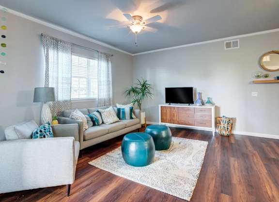 A living room with a white couch, a blue ottoman, and a wooden floor.at Century Ariva, Lakeland, 33812