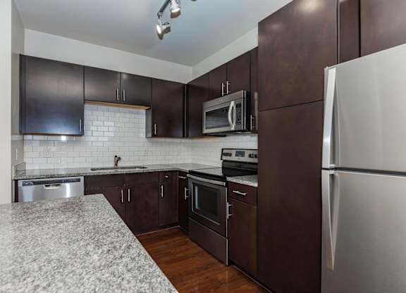 A kitchen with dark brown cabinets and a granite countertop.at Century Cedar Hill, Cedar Hill