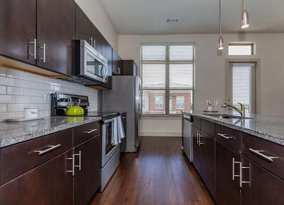 A kitchen with dark wood cabinets and a granite countertop.at Century Cedar Hill, Cedar Hill, 75104
