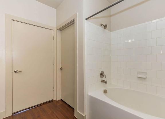 A white tiled bathroom with a bathtub and a door.at Century Cedar Hill, Texas