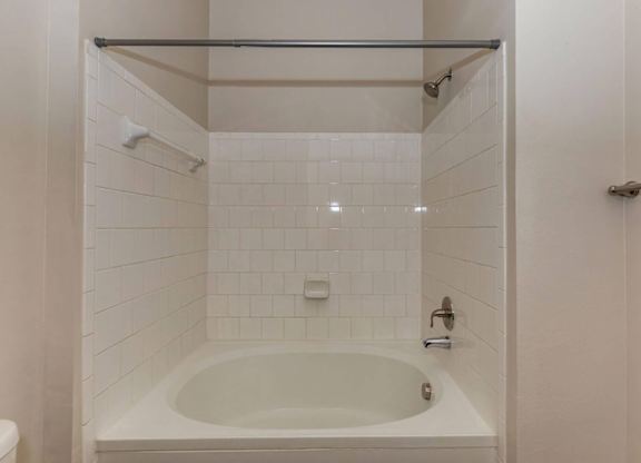 A white tiled bathroom with a white bathtub and a white toilet.at Century Cedar Hill, Cedar Hill, TX 75104