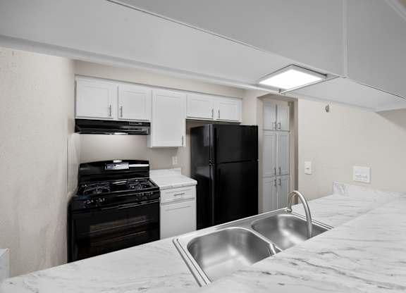 A kitchen with a black refrigerator, white oven, and a stainless steel sink.