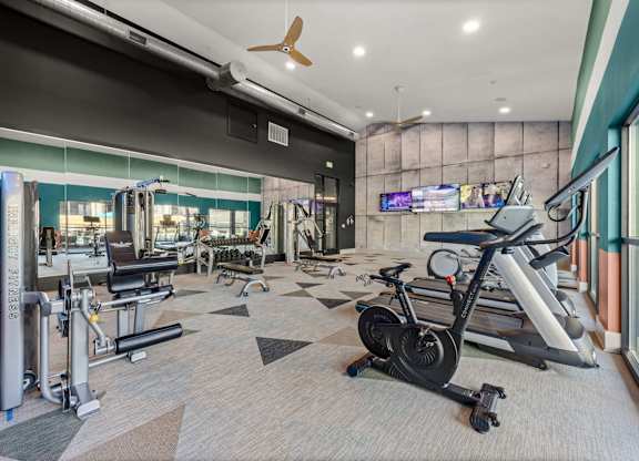 A gym with a variety of equipment including treadmills, weights, and a television. at Bridge at Tech Crossing, Austin, 78753