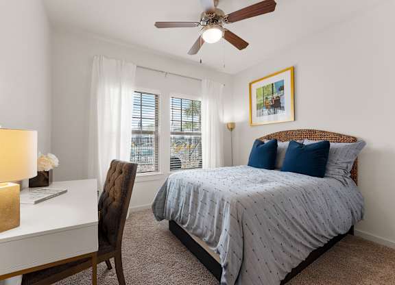 A bedroom with a bed, desk, chair, and window.