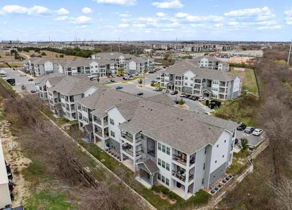 An aerial view of a large apartment complex with multiple buildings and cars parked in the parking lot.