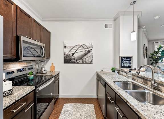 A kitchen with a black granite countertop and a white sink. at Bridge at Indigo, Austin, TX, 78717