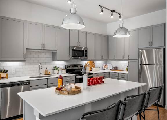 A modern kitchen with a white island and grey cabinets. at The Haywood Apartments, Texas
