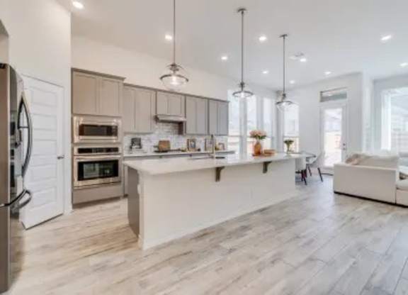 A modern kitchen with a refrigerator on the left and a dining area with a white sofa.
