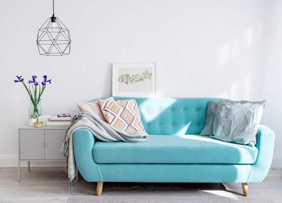 A blue couch with a pillow and a blanket on it.