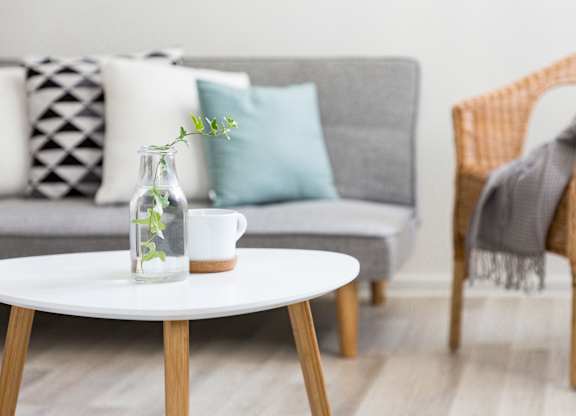 A living room with a grey couch, a white coffee table, and a wicker chair.