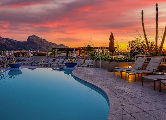 A poolside area with lounge chairs and a mountain in the background during sunset.