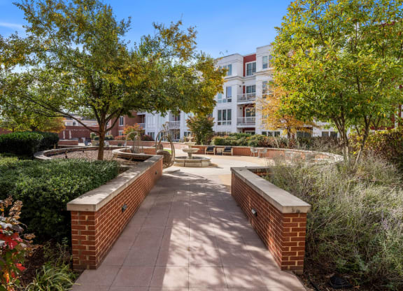 a walkway with benches and trees in front of an apartment building