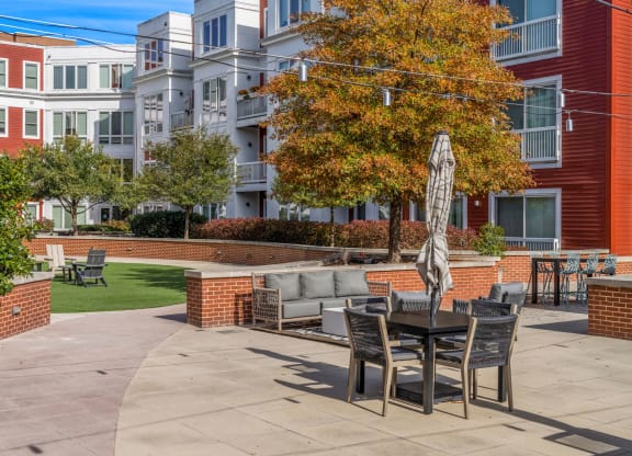 A patio with a table and chairs is surrounded by a brick wall and a tree.