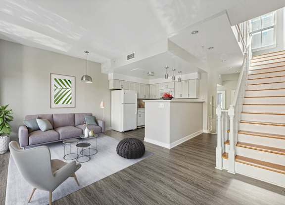 A living room with a grey sofa and a white kitchen in the background.