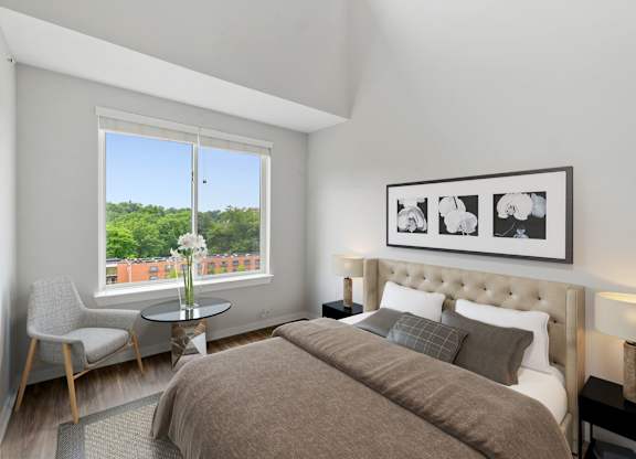 A bedroom with a large bed, a chair, a table, and a framed picture on the wall.
