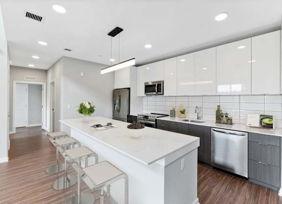 A modern kitchen with a long white island and stainless steel appliances.