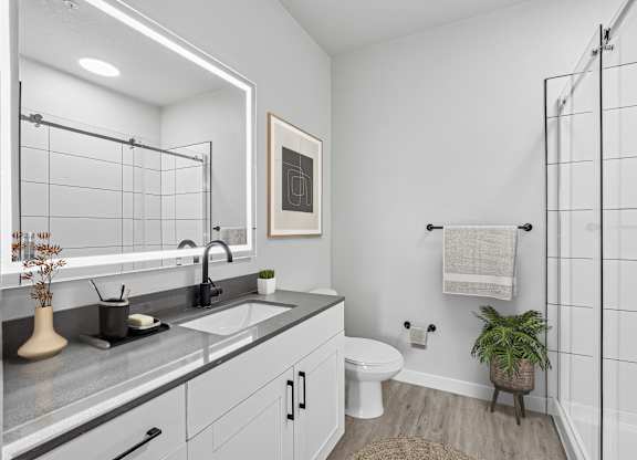Model apartment bathroom with walk-in shower and backlit mirror