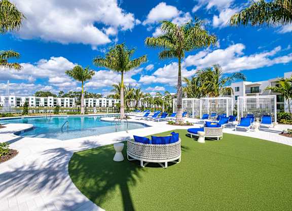 A pool surrounded by palm trees and lounge chairs.