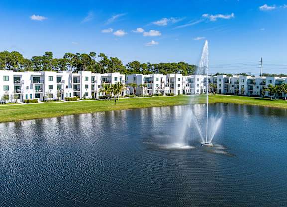 A fountain in the middle of a lake in front of apartment buildings.
