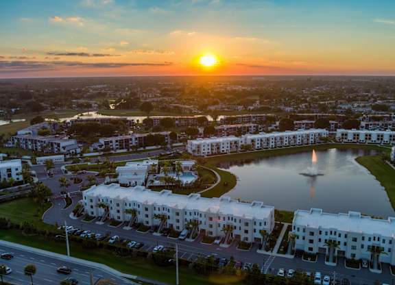 A sunset view of a residential area with a large white building and a fountain in the foreground.